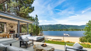 Eine Terrasse mit Sitzgelegenheiten im Freien, einer Steinkaminfeuerstelle und Blick auf einen See und Berge.