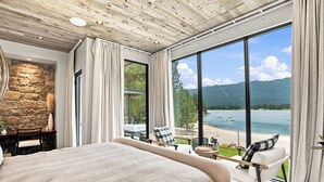 Ein Schlafzimmer mit einem großen Bett, einer Steinwand, Blick auf einen See und einem Sessel am Fenster.