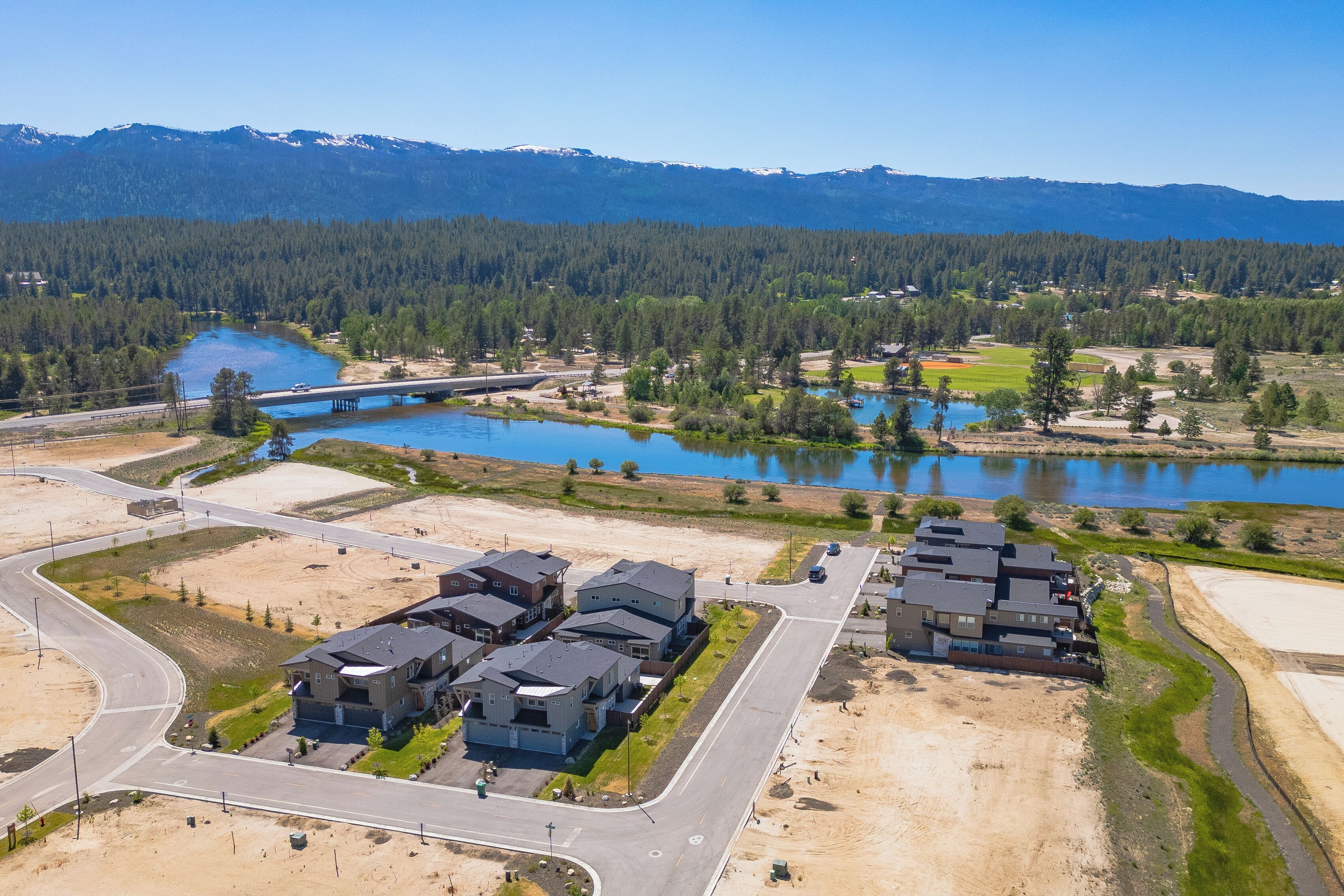A residential area with modern houses, a lake, and a forested mountain range in the background.