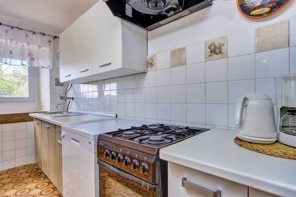 A compact kitchen with white cabinets, a gas stove, a sink, and a coffee maker.