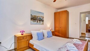 Un dormitorio con cama, armario de madera, lámparas de noche, un cuadro y un baño visible a través de una puerta abierta.