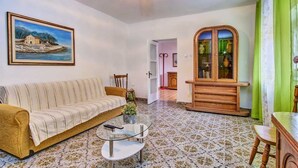 Un salón con un sofá, una mesa de centro de vidrio, un mueble de madera con puertas de cristal, un cuadro en la pared y un suelo estampado.