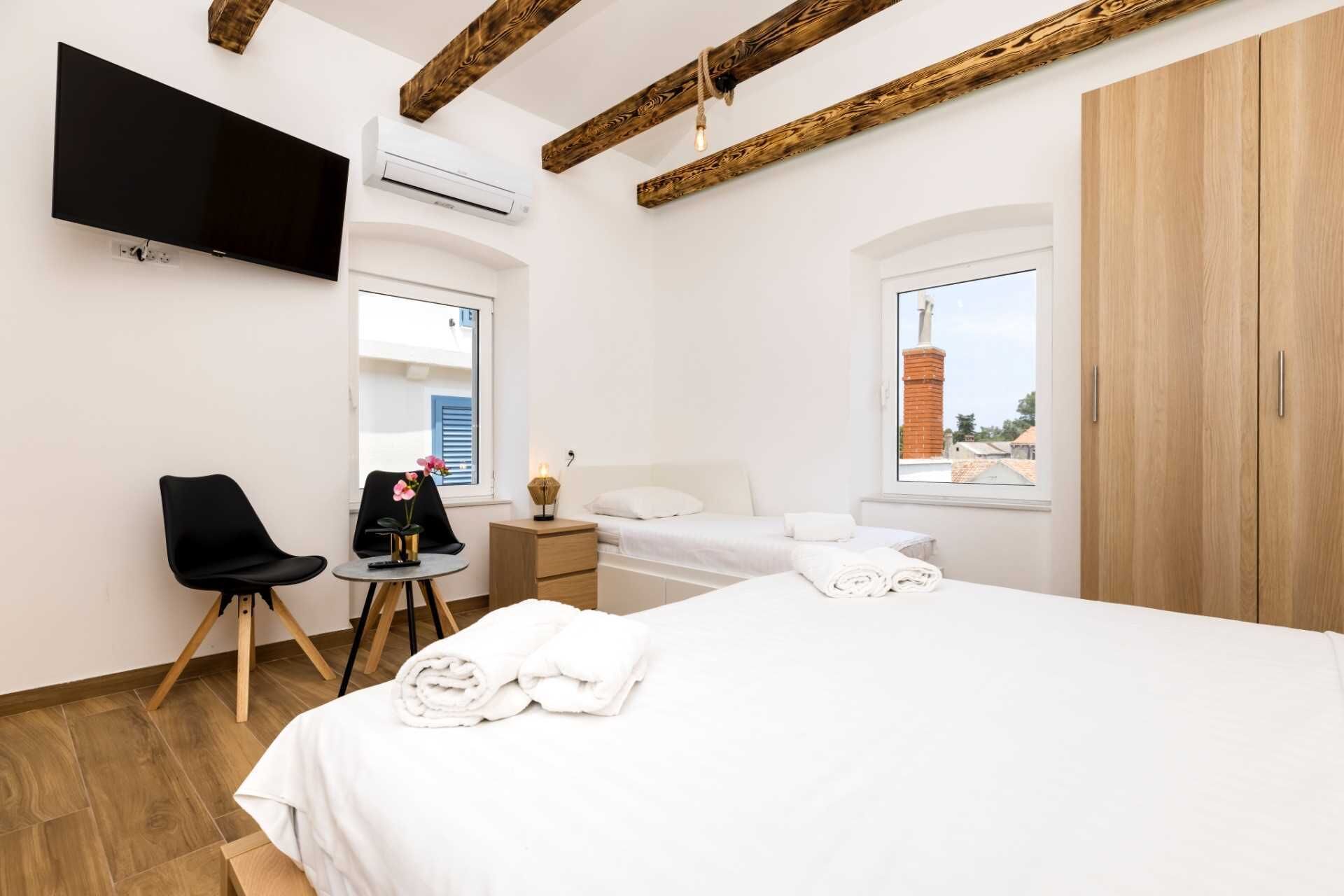 Ein Hotelzimmer mit zwei Betten, einem Fernseher, einer Klimaanlage, einem Schreibtisch mit Stuhl und einem Fenster mit Blick nach draußen.