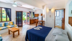 Une chambre d’hôtel comprenant un lit, un canapé, une table à manger, un coin cuisine et une porte-fenêtre coulissante donnant sur un balcon.