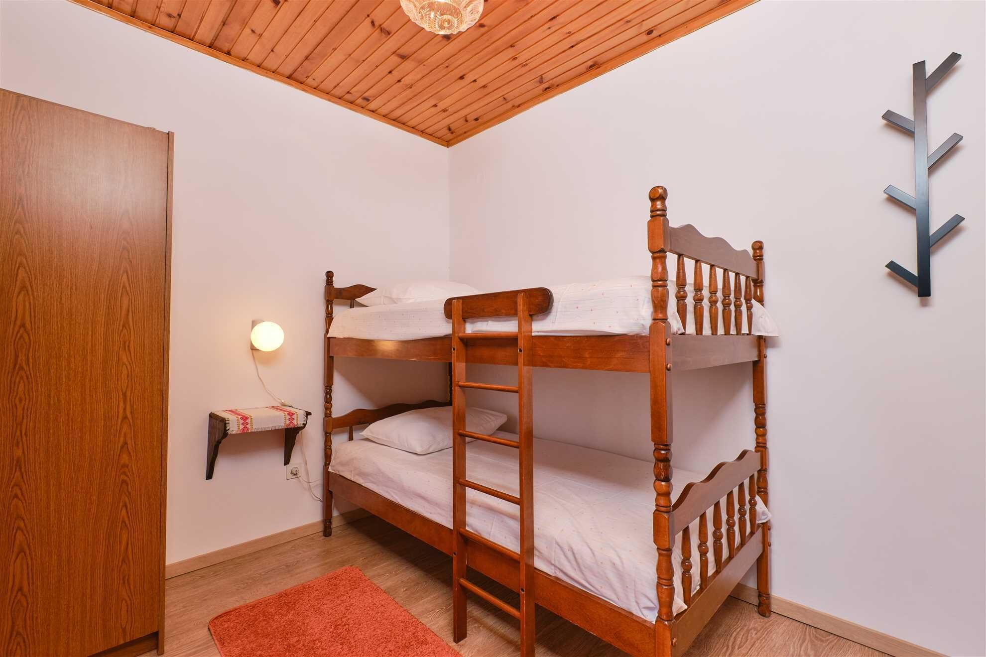 Een slaapkamer met stapelbed, houten plafond, een wandlamp en een rood tapijt.