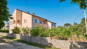 A two-story house with a stone wall in front, a gravel driveway, and a vineyard with grapevines. - Charming 2-Bedrooms Apartment in Nerezine (Nerezine)