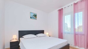 A bedroom with a bed, two bedside tables with lamps, a window with pink curtains, and a small painting on the wall. - Charming 2-Bedrooms Apartment in Nerezine (Nerezine)