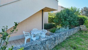 A patio with a table and chairs, a stone wall, and greenery. - Charming 2-Bedrooms Apartment in Nerezine (Nerezine)