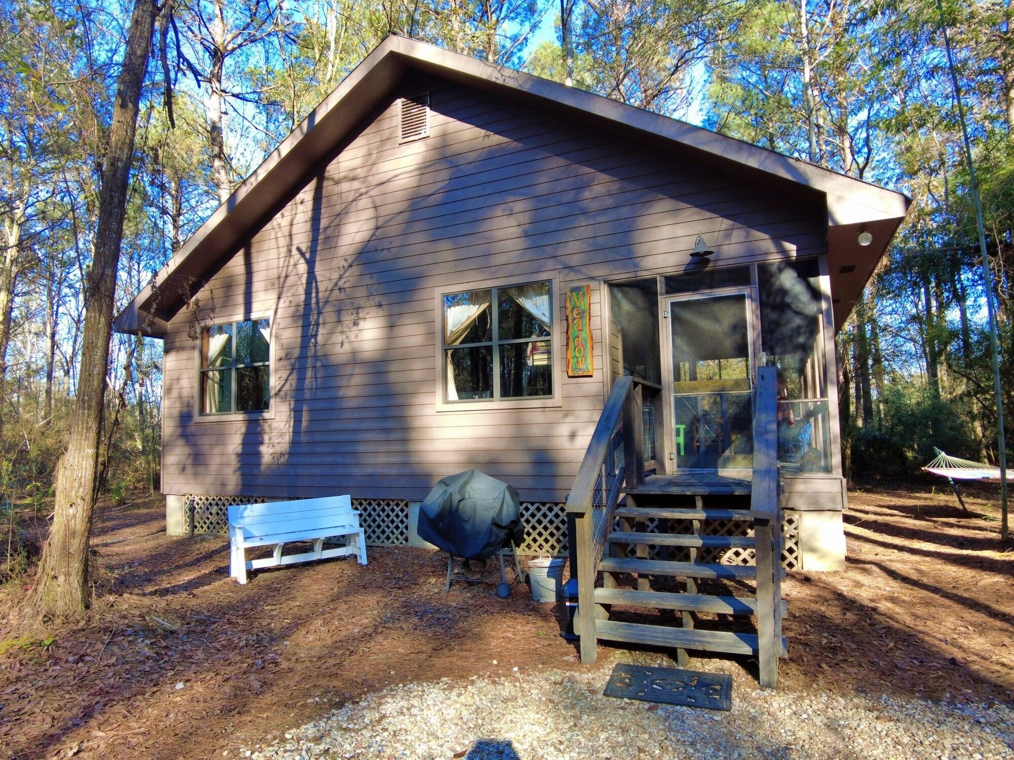 A cabin with a covered porch, a small deck, and a bench.