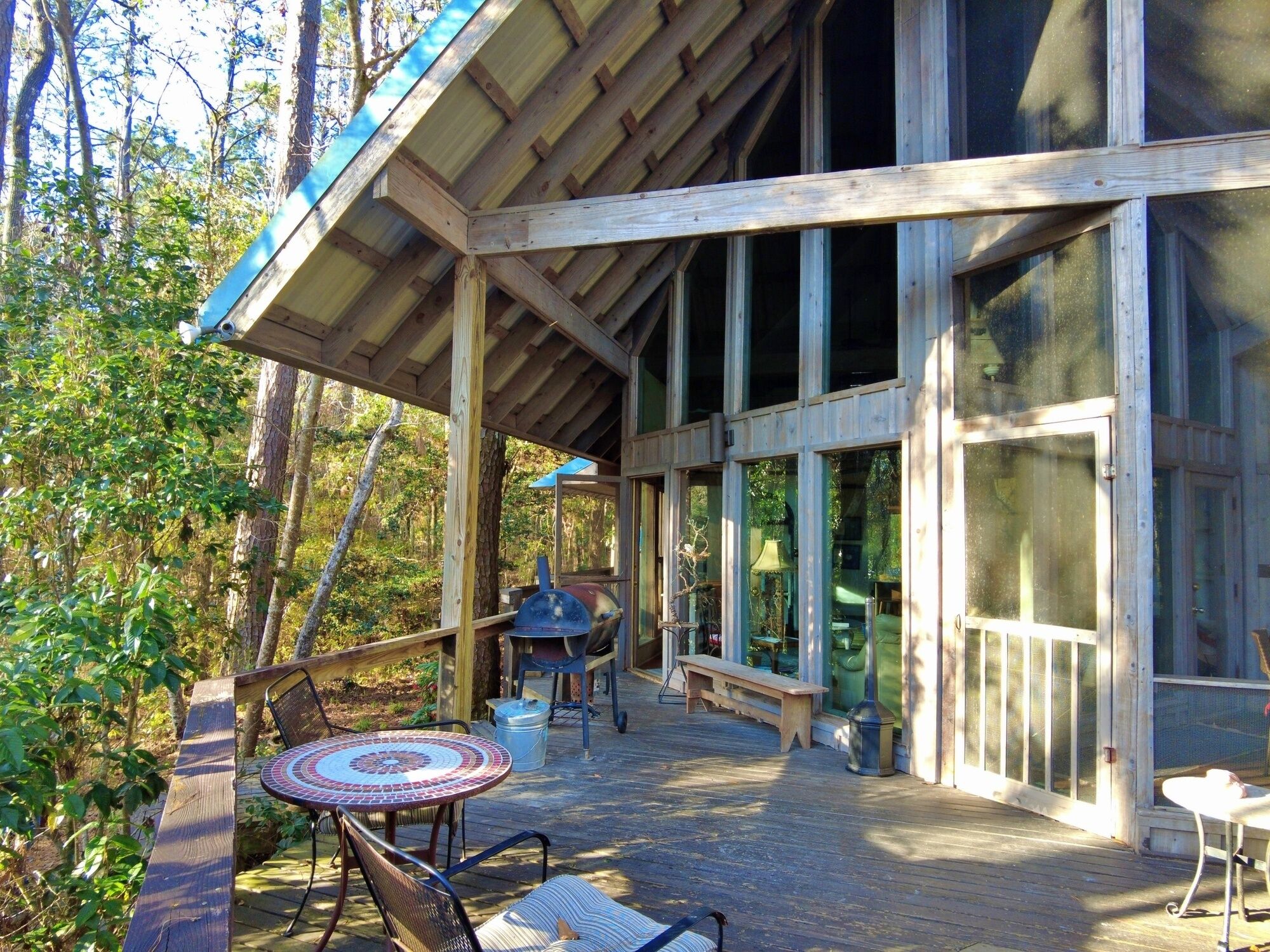 Une terrasse en bois dotée d’un espace salon abrité, de grandes fenêtres et d’une vue sur la forêt environnante.