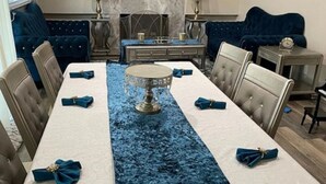 Ein Esszimmer mit einem langen Tisch, gedeckt für sechs Personen, einem blauen Sammlaufschal und einem zentralen Dekostück.