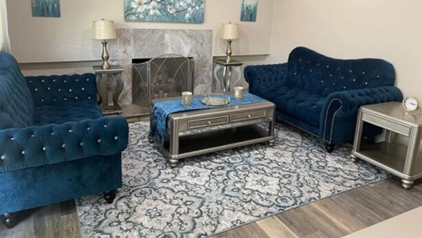 Ein Wohnzimmer mit zwei blauen Sofas, einem gemusterten Teppich, einem Kamin und Wandbildern.