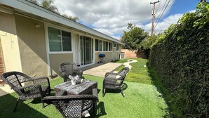 Eine Terrasse mit Tisch, Stühlen, einem Grill und einer Hecke.