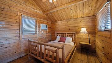 Ein Zimmer in einer Holzhütte mit einem Bett, einem Deckenventilator und einem Fenster mit Jalousien.