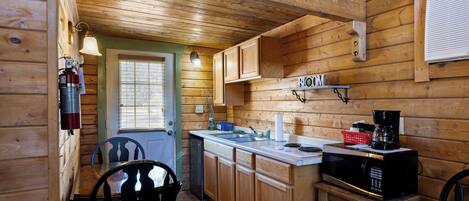 Cocina de cabaña de madera con una mesa y sillas de comedor, un microondas y un lavamanos.
