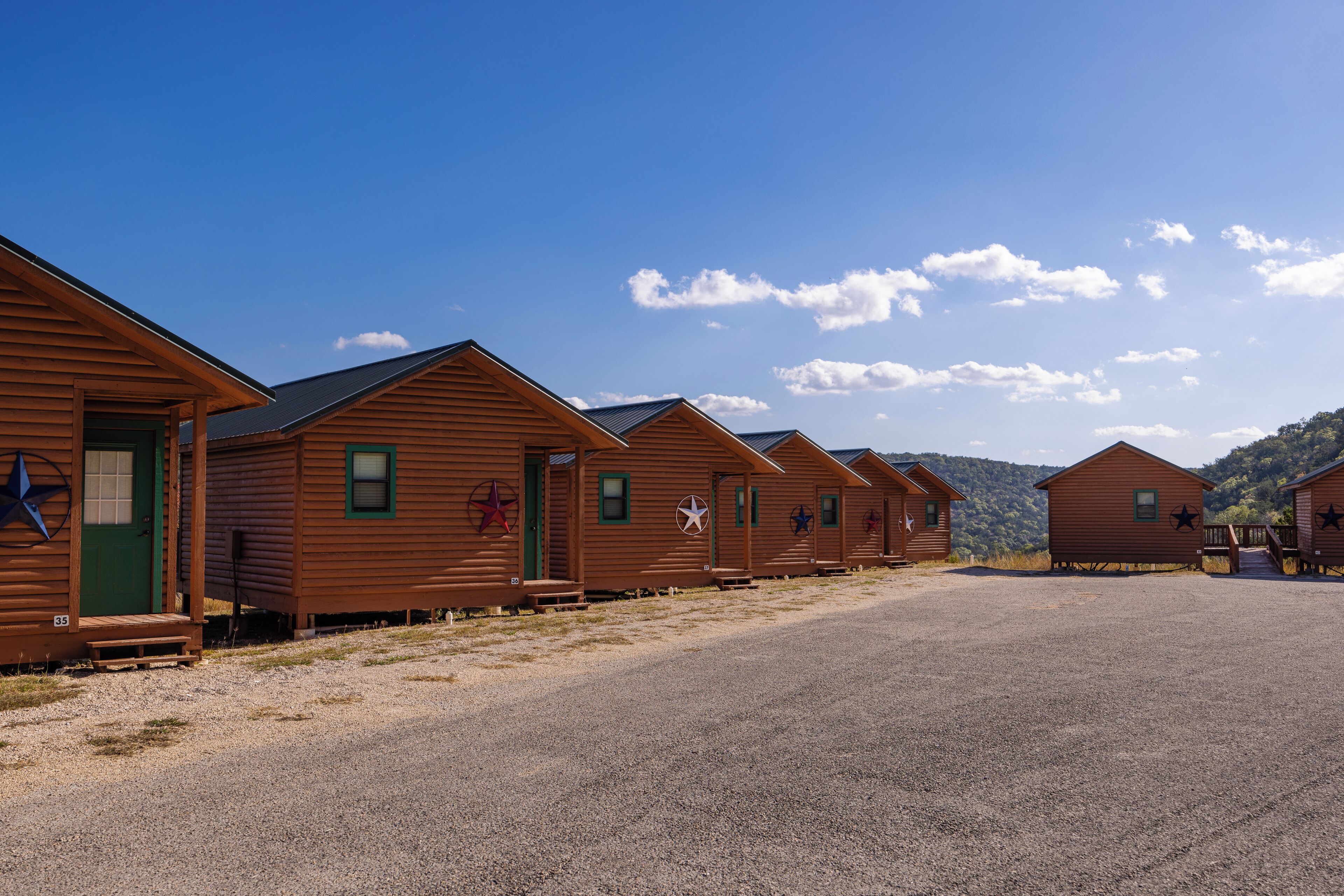 A row of wooden cabins with star decorations, a gravel driveway, and a clear blue sky.