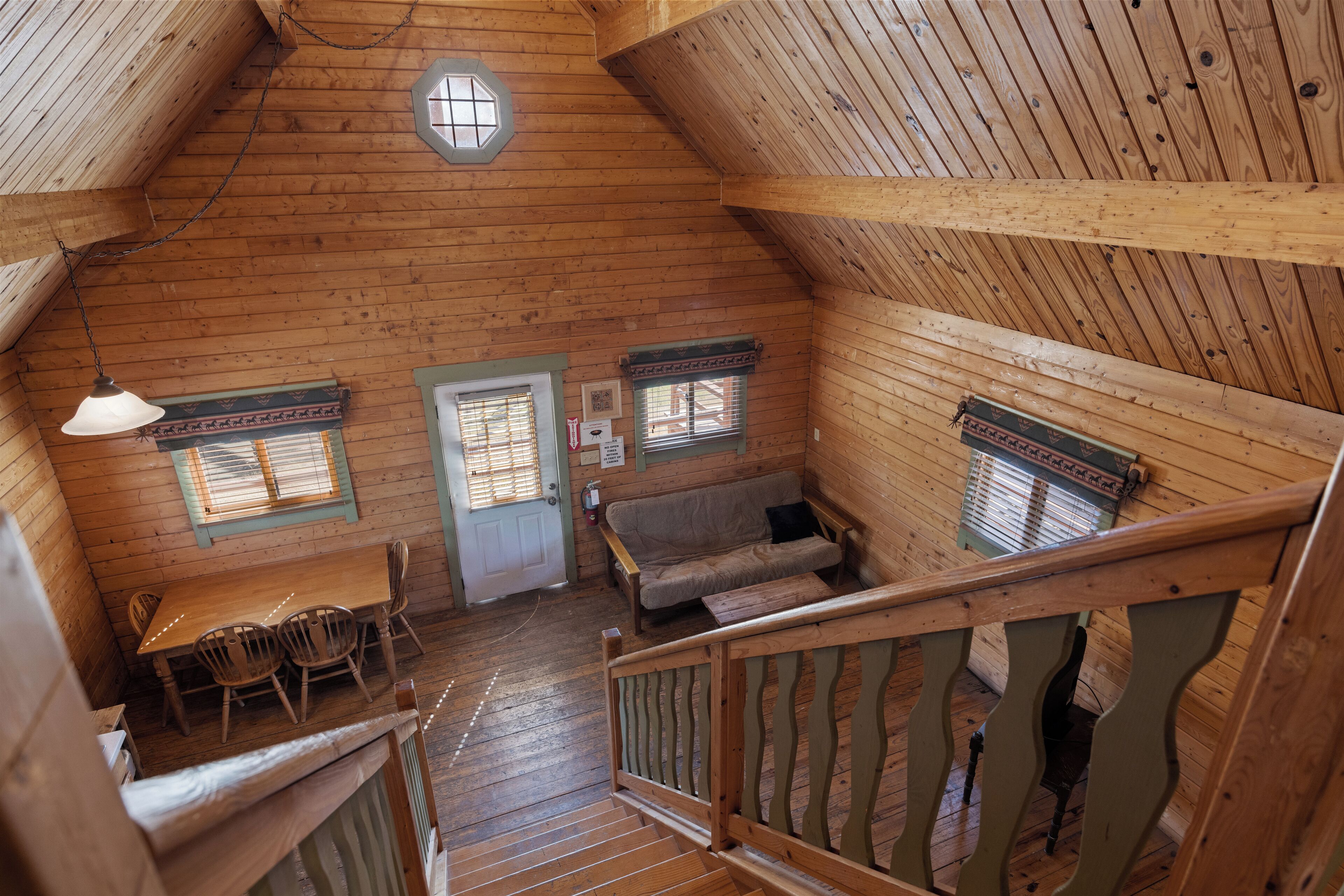 A wooden interior with a dining area, a sofa, and a staircase.