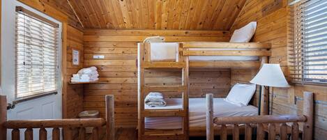 A wooden cabin with bunk beds, a small shelf with towels, and a window with blinds.