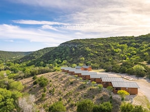 A row of cabins with a dirt path leading to a communal area, surrounded by forested hills. - Texas Hill Country Resort (Medina)