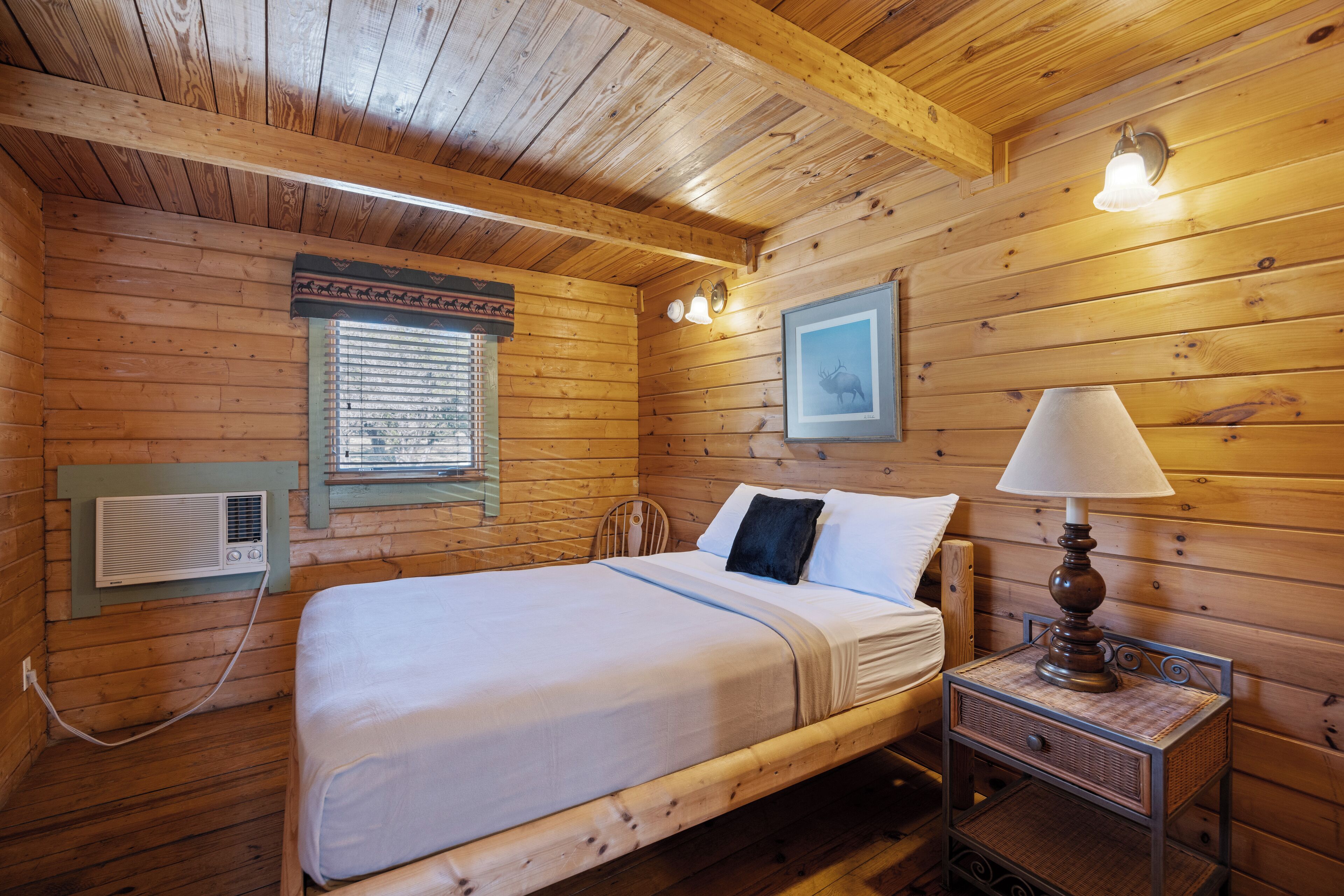 A wooden cabin bedroom with a bed, bedside lamp, and a framed picture on the wall.