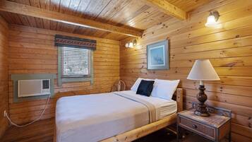 A wooden cabin bedroom with a bed, bedside lamp, and a framed picture on the wall.