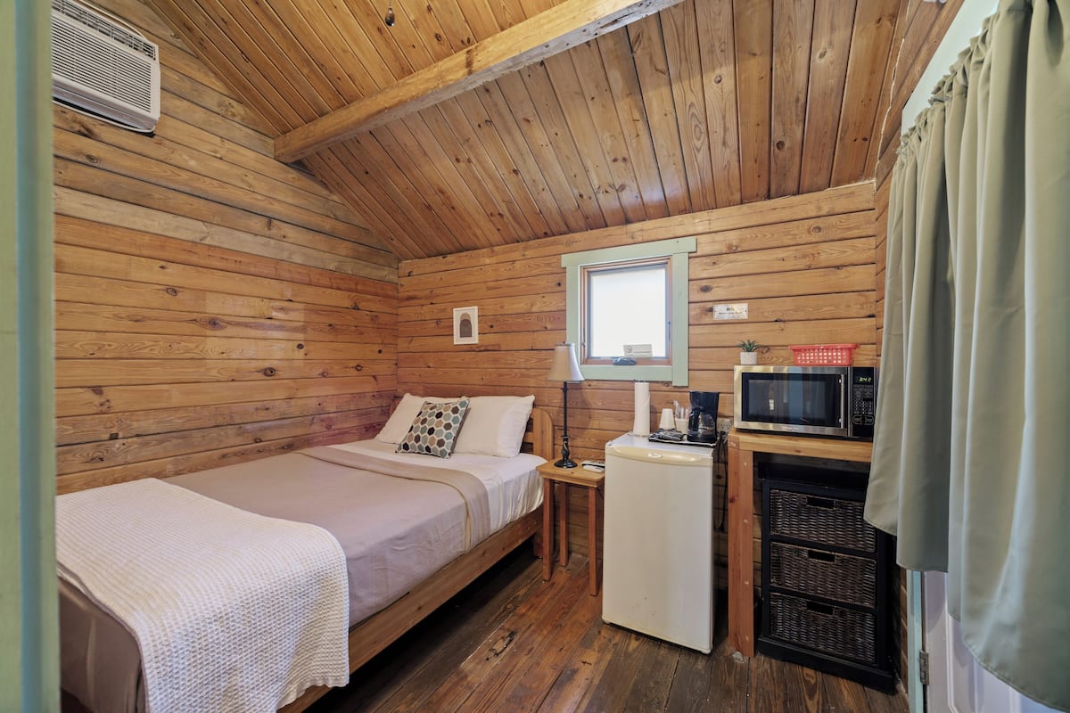 A small cabin with two single beds, a compact kitchenette with a microwave, and a window with curtains.