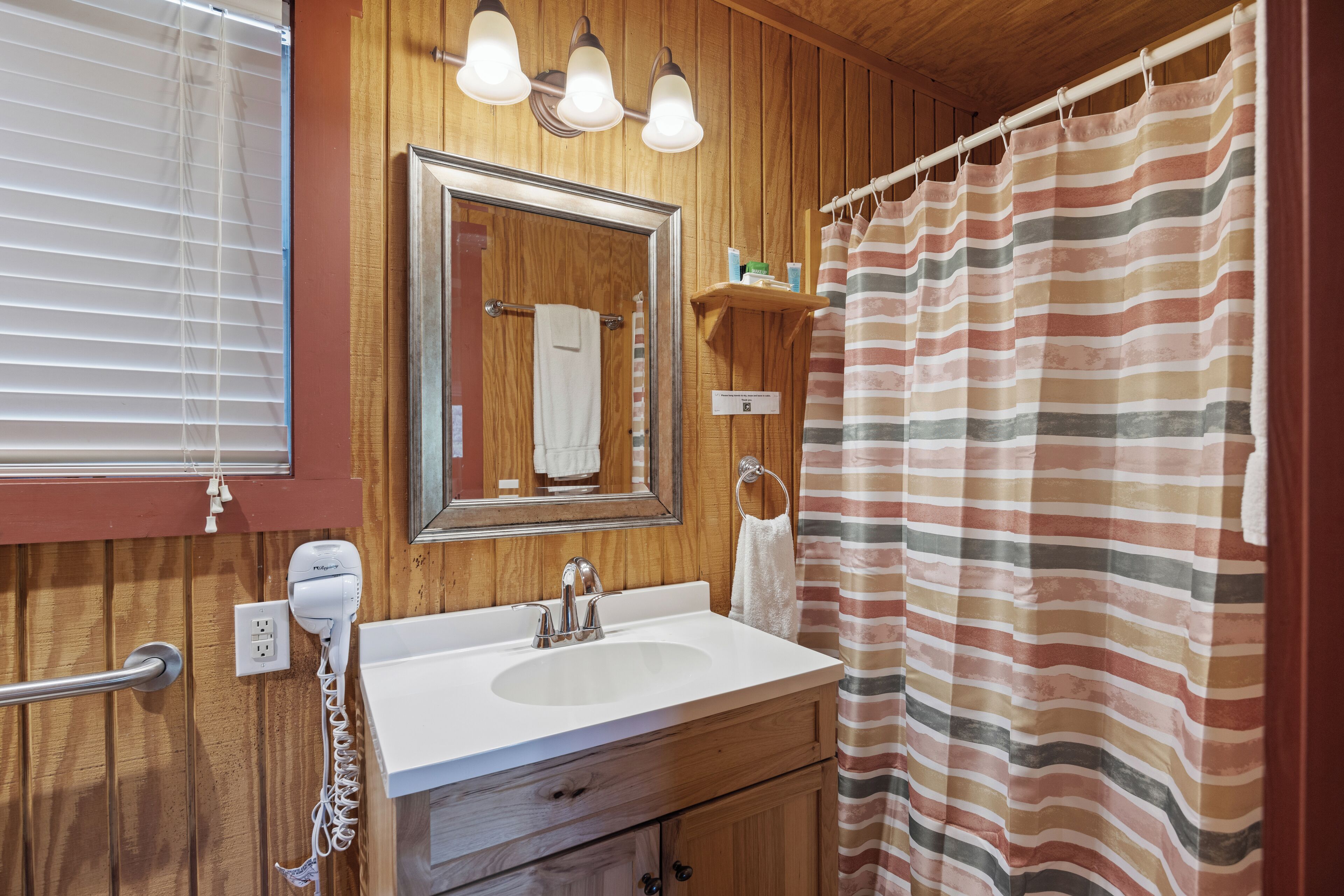 A bathroom with a wooden vanity, a sink, a mirror, a towel rack, a shower curtain, and a hairdryer.