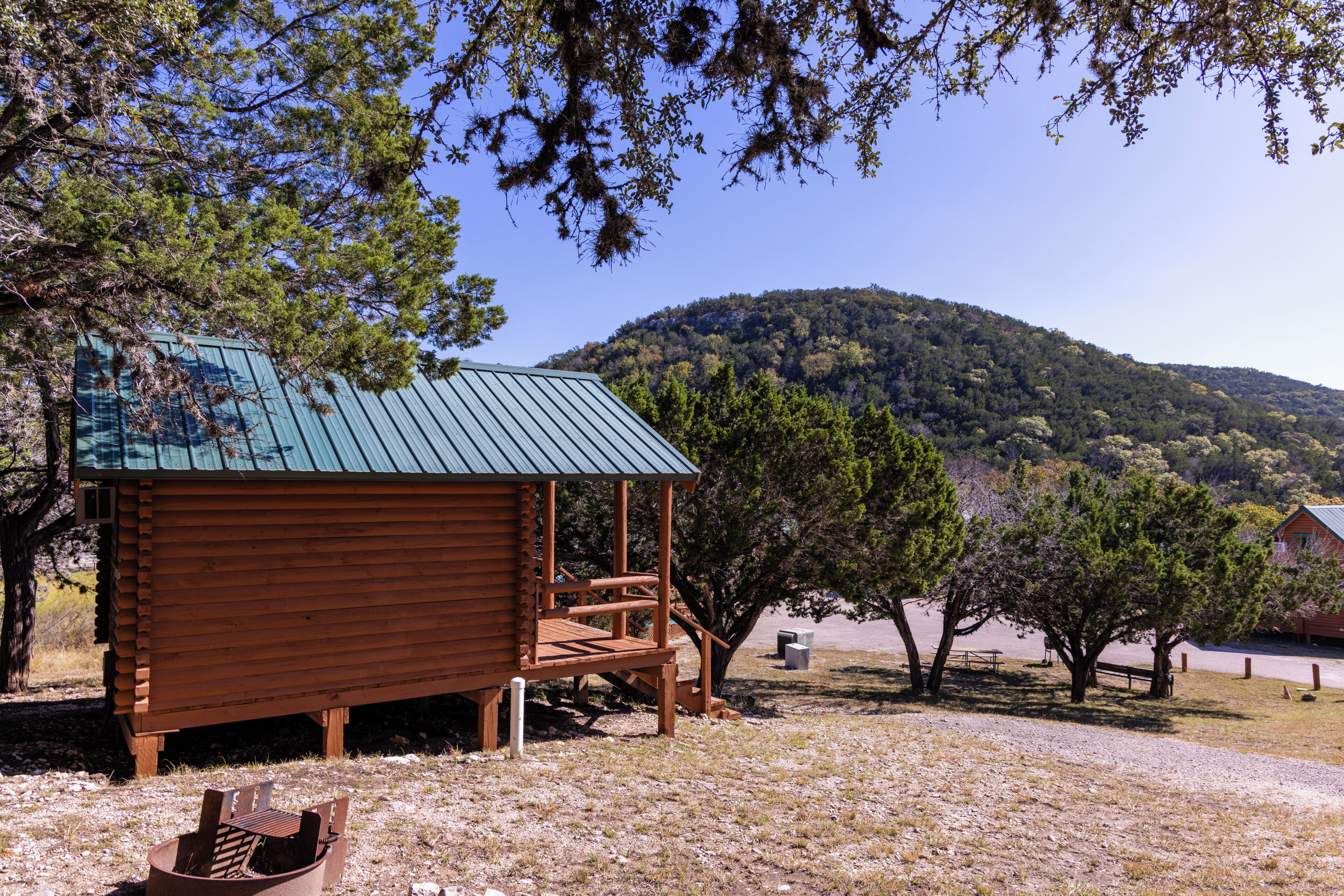 A rustic cabin with a metal roof, wooden deck, and a view of a forested hill.