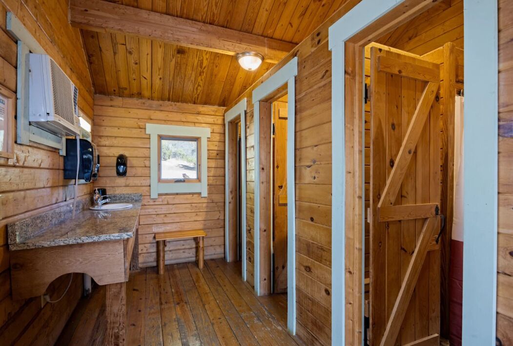 Interior de una cabaña de madera con cocina, un banco y una puerta que da a otra habitación.