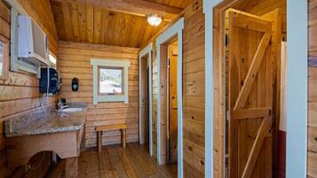 Interior de una cabaña de madera con cocina, un banco y una puerta que da a otra habitación.