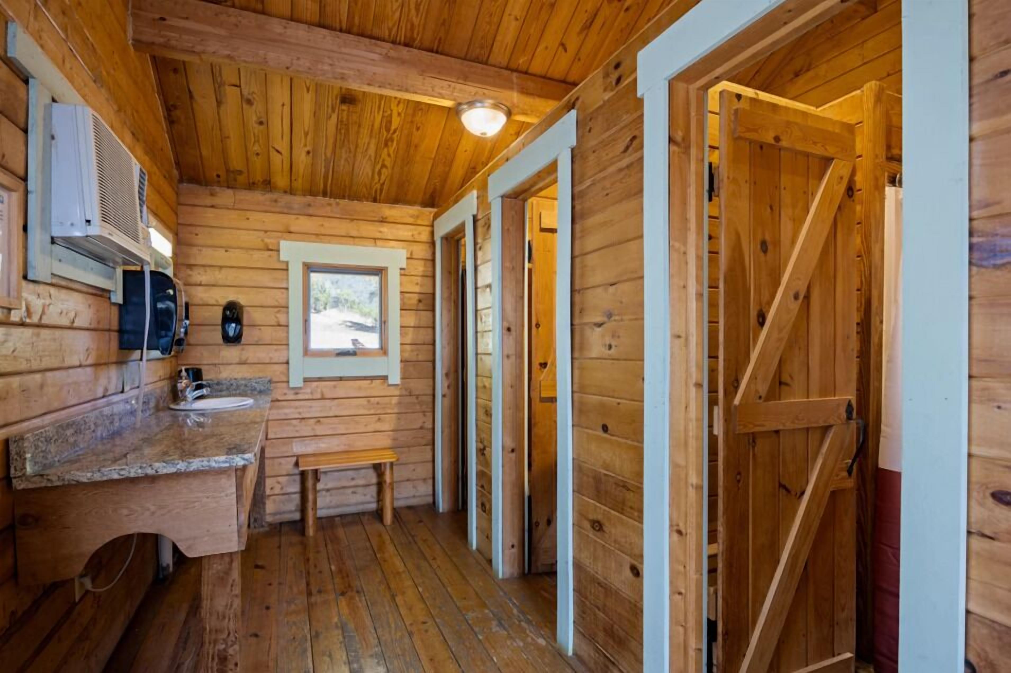 A wooden cabin interior with a wooden floor, a bench, a sink, and a door.