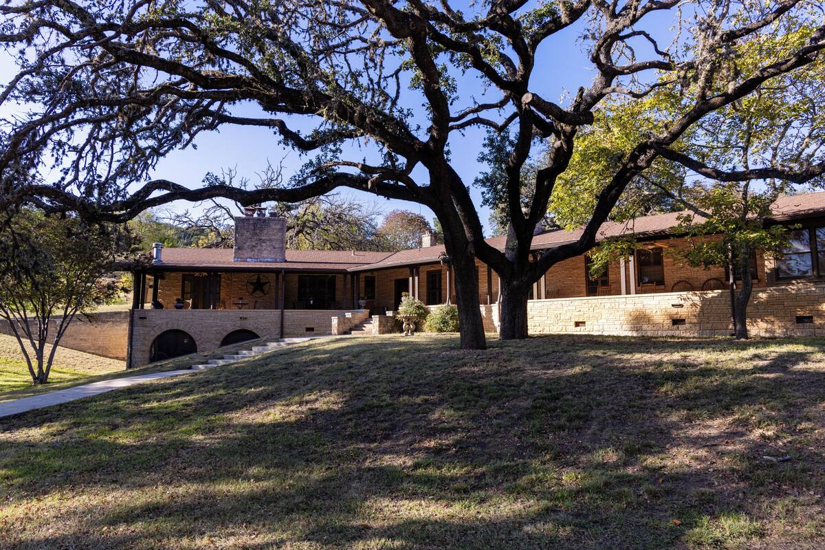 A building with a brick exterior, a covered porch, and a large tree in front.
