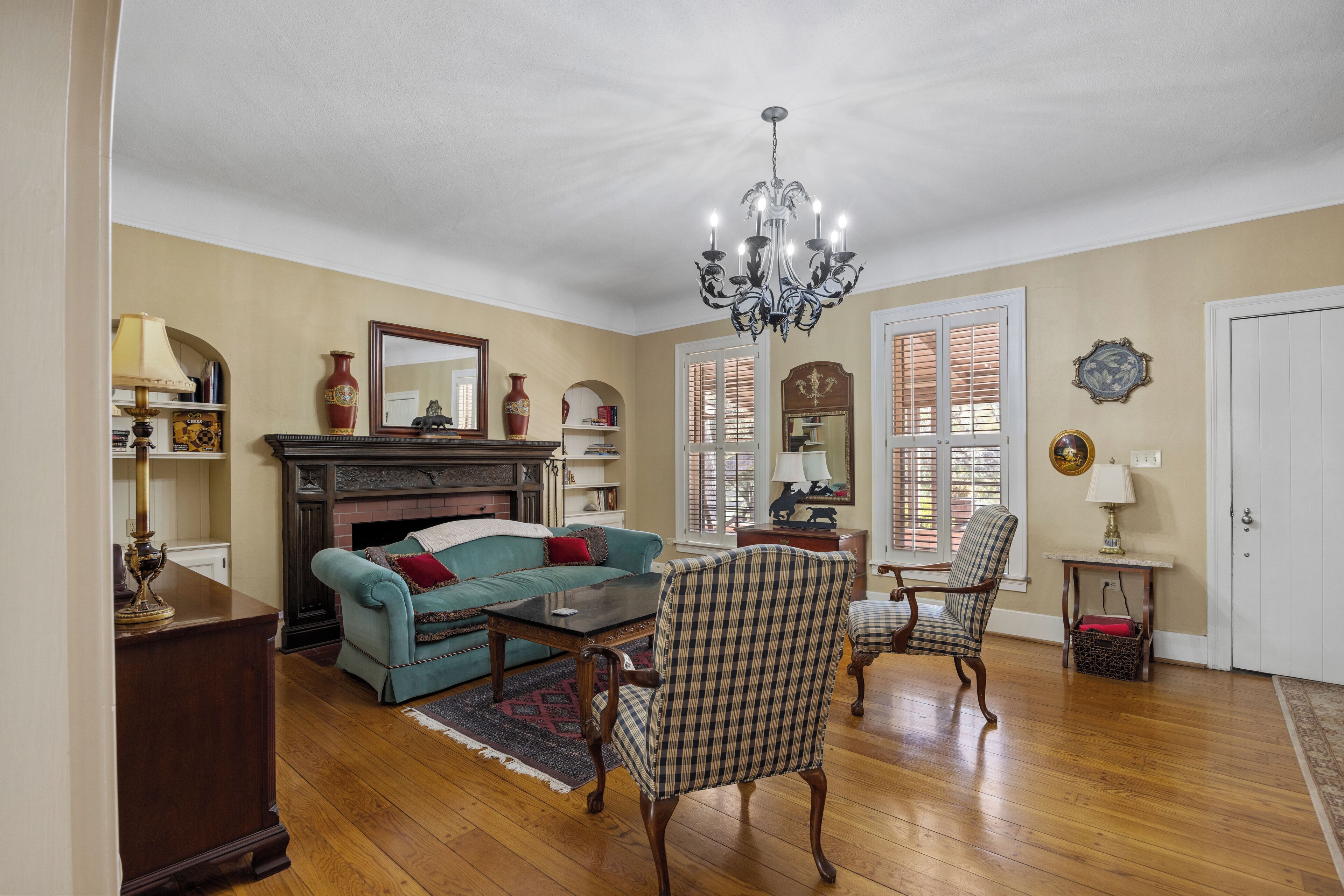 A spacious living room with a fireplace, a chandelier, and a large mirror.