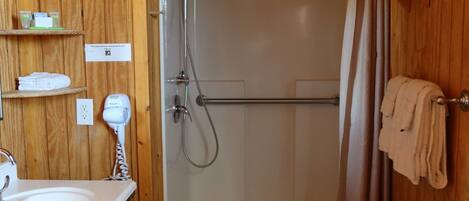 A wooden-paneled bathroom with a sink, a hairdryer, a shower with a curtain, and a towel rack.