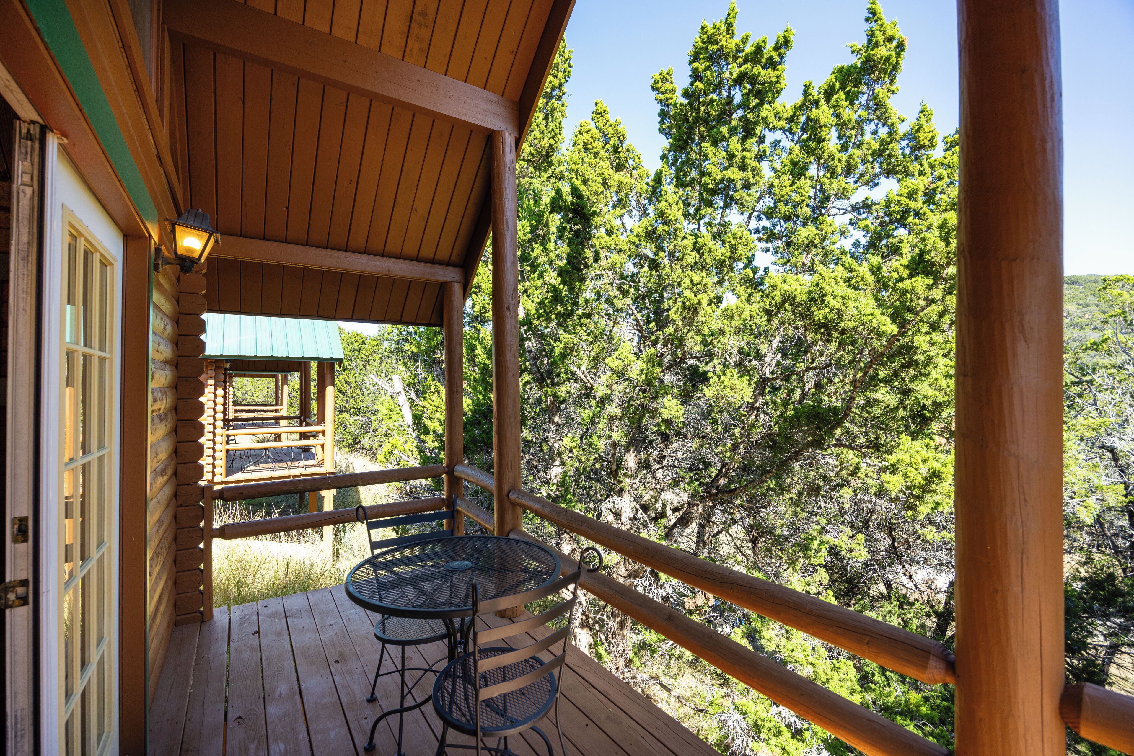 Terraza de madera con mesa y sillas, con vista a un área boscosa.
