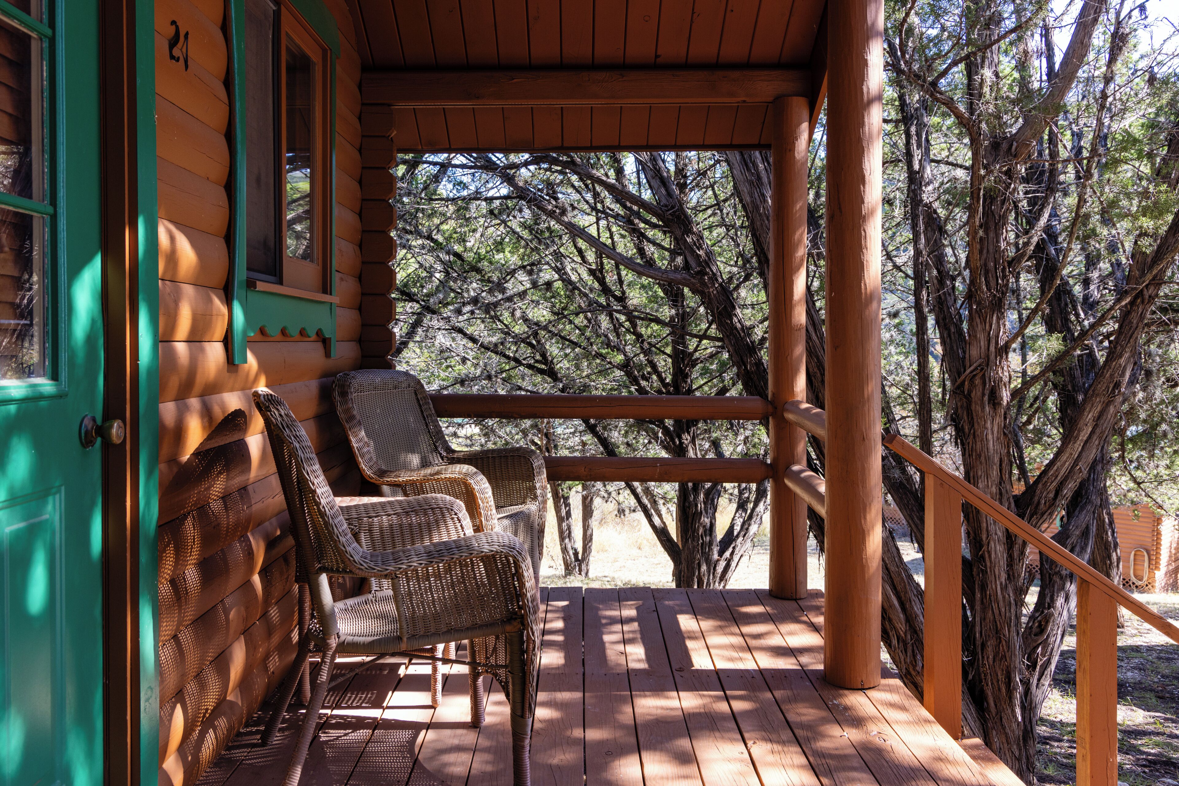 A wooden porch with wicker chairs, a wooden railing, and a view of trees.