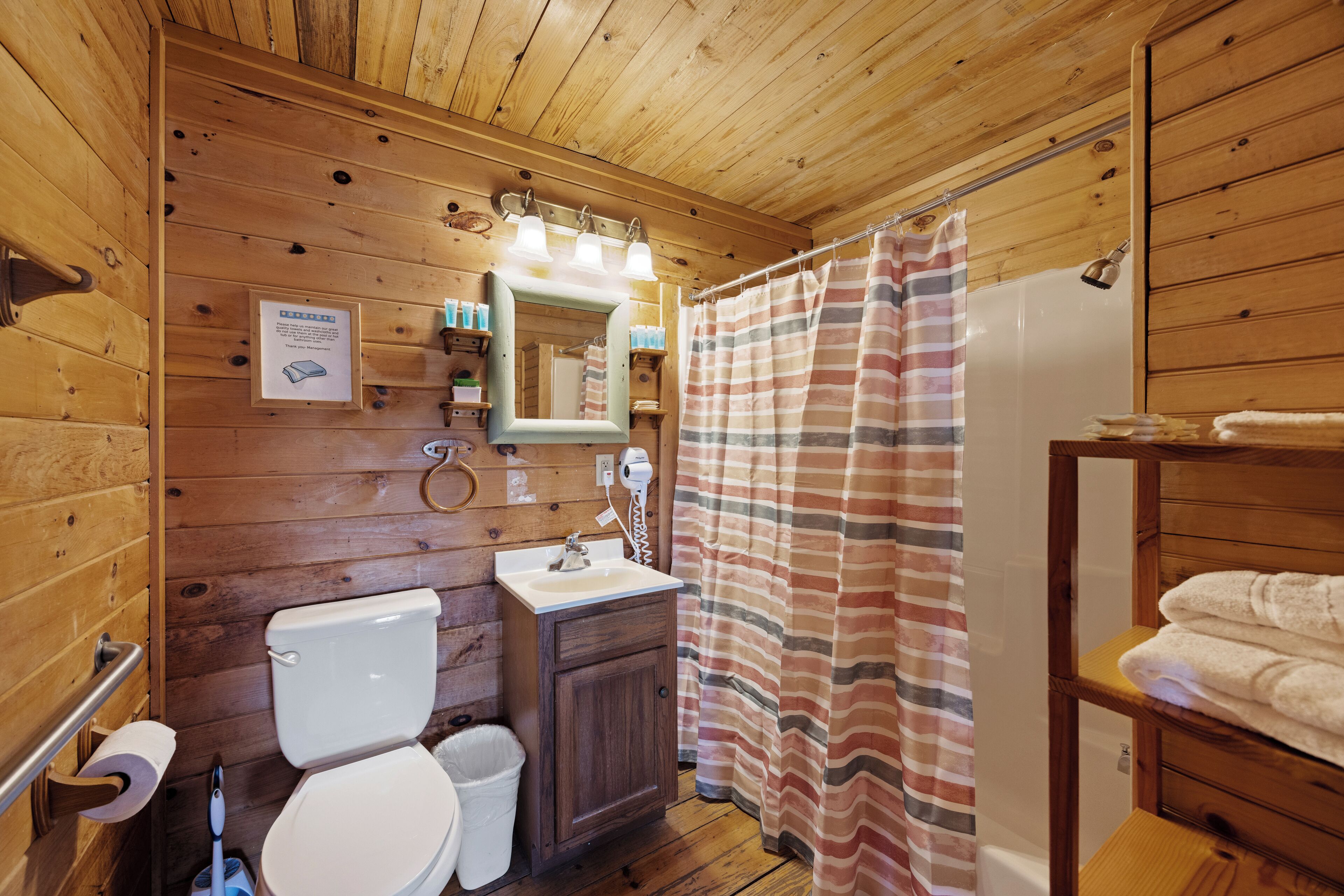 A wooden cabin bathroom with a toilet, sink, and shower.