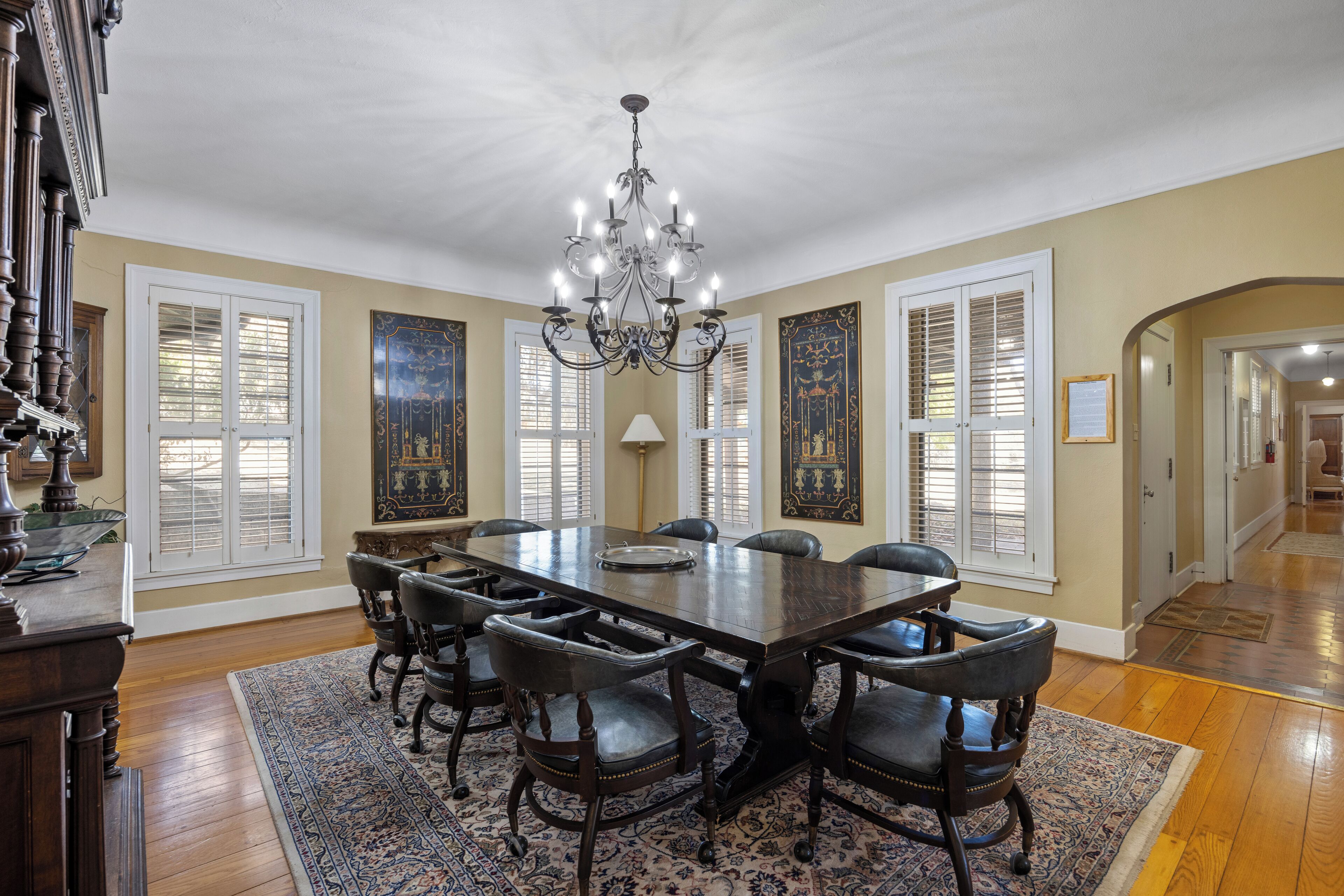 Une salle à manger élégante, avec une grande table en bois, six chaises, un lustre et des panneaux décoratifs sur les murs.