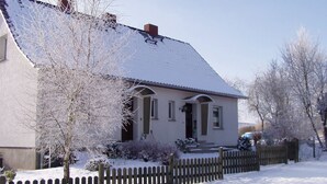 Una casa de dos pisos con techo nevado y valla de piquetes de madera al frente.