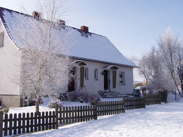 Una casa de dos pisos con techo nevado y valla de piquetes de madera al frente.