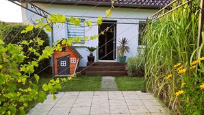 Una casa con un jardín pequeño, una casita de juegos de madera y una planta en maceta.