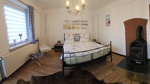 Un dormitorio con cama, una silla, chimenea y ventana con cortinas.