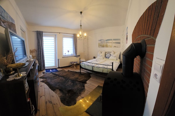 A bedroom with a bed, a television, a fireplace, and a window with curtains.