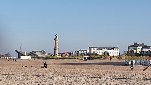 Una playa con un faro destacado, edificios modernos y un paisaje arenoso.