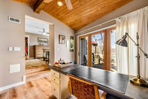 Una cocina con techo de madera, un comedor con mesa y sillas, y vistas al exterior a través de grandes ventanales.