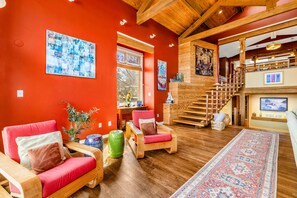 Amplia sala de estar con pared roja, muebles de madera, una escalera y obras de arte.