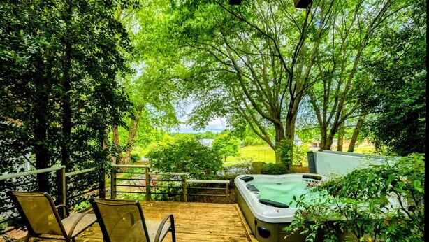 Eine Holzterrasse mit Whirlpool, Stühlen und Blick auf einen üppigen Garten.