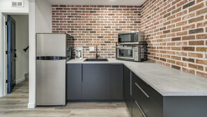 Une cuisine compacte avec un mur de briques en guise de crédence, des appareils en acier inoxydable et des meubles de couleur sombre.