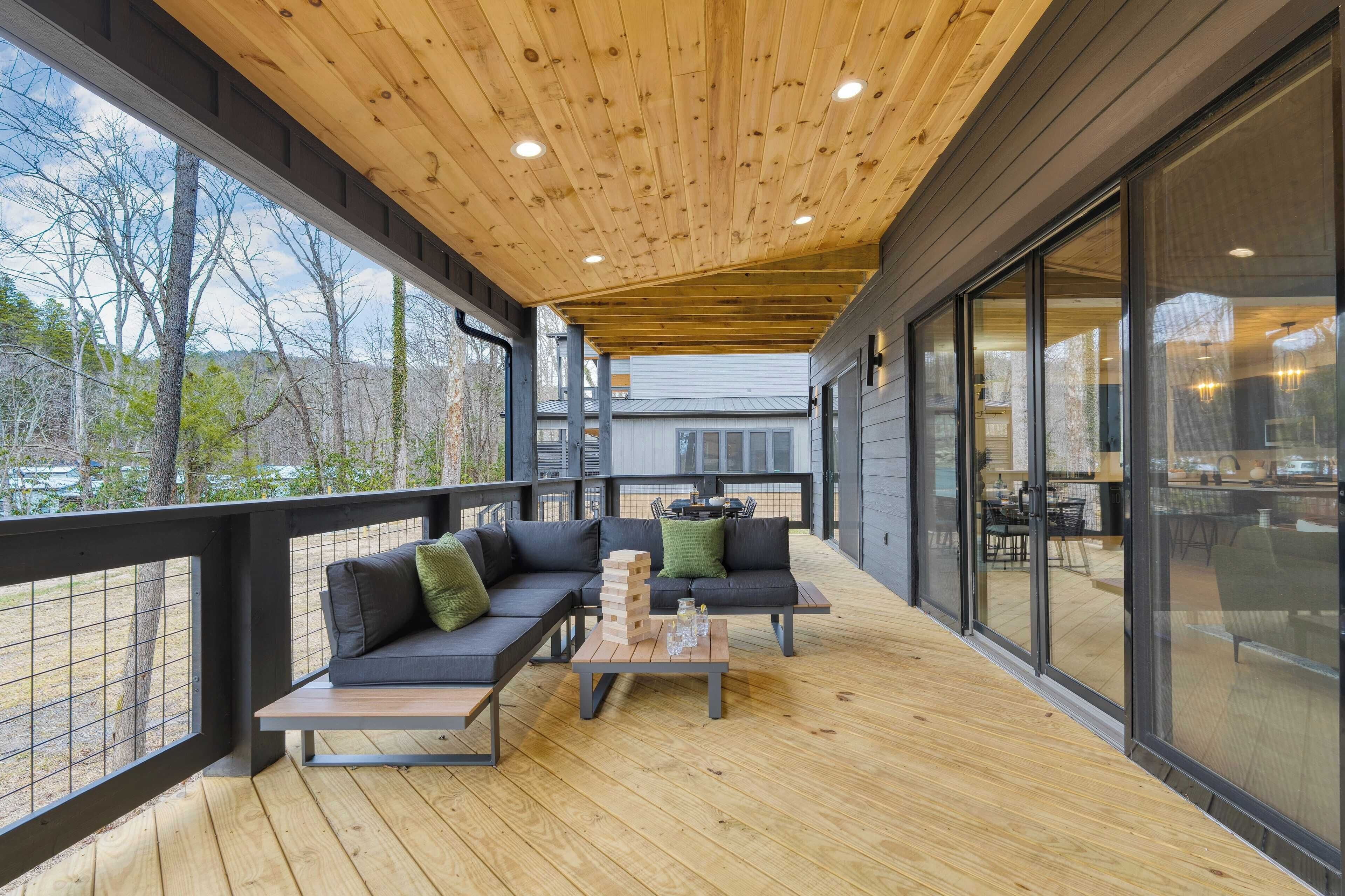 A covered outdoor deck with a wooden ceiling, a sofa, a coffee table, and a view of the surrounding area.