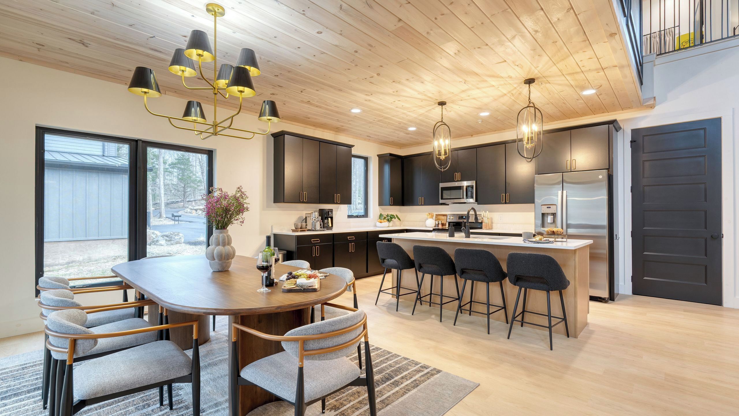 A modern kitchen with dark cabinetry, a central island with bar stools, a dining table with chairs, and a chandelier.